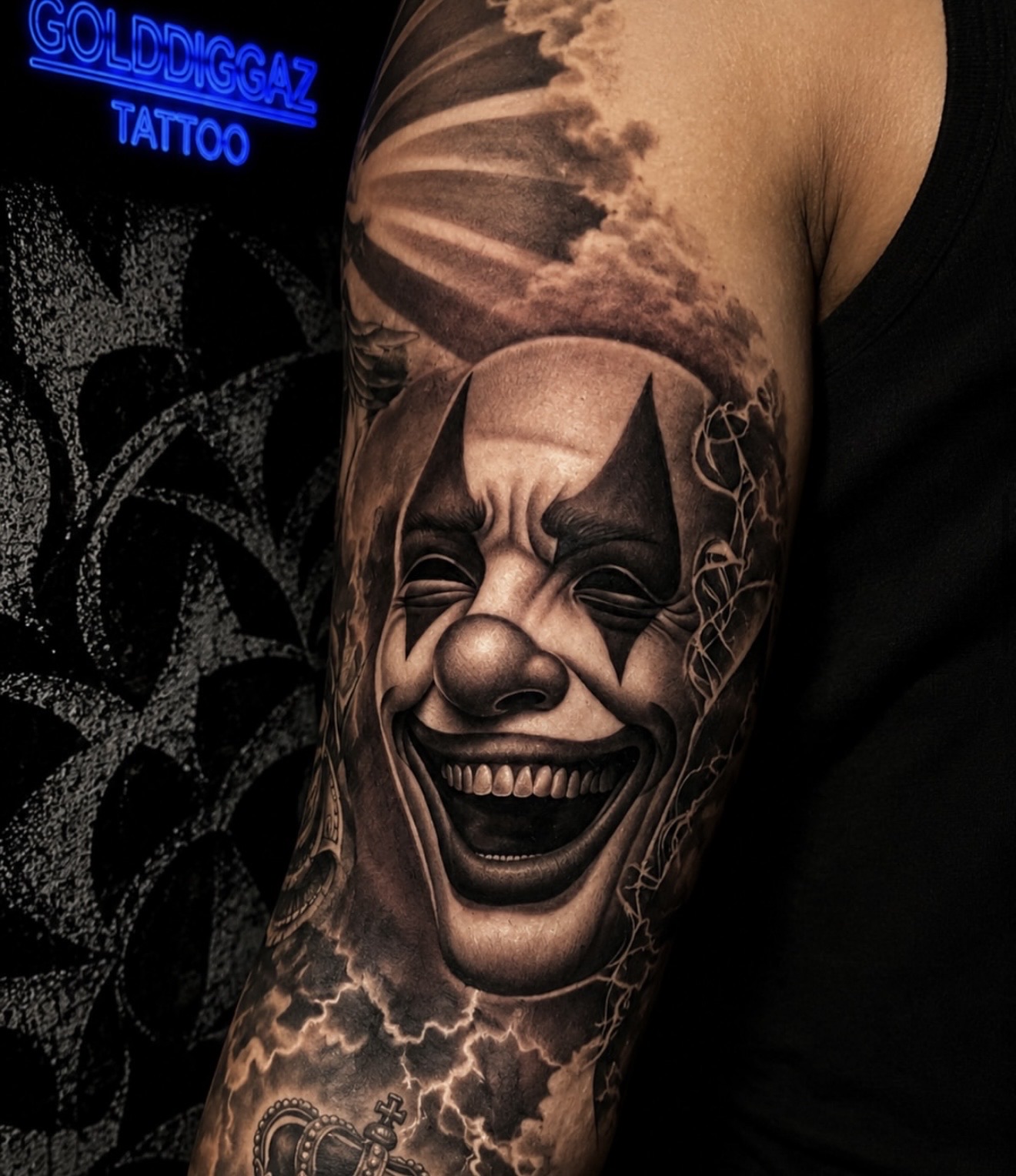 Lachender Clown in Black and Grey auf dem Oberarm, mit Wolken und Krone